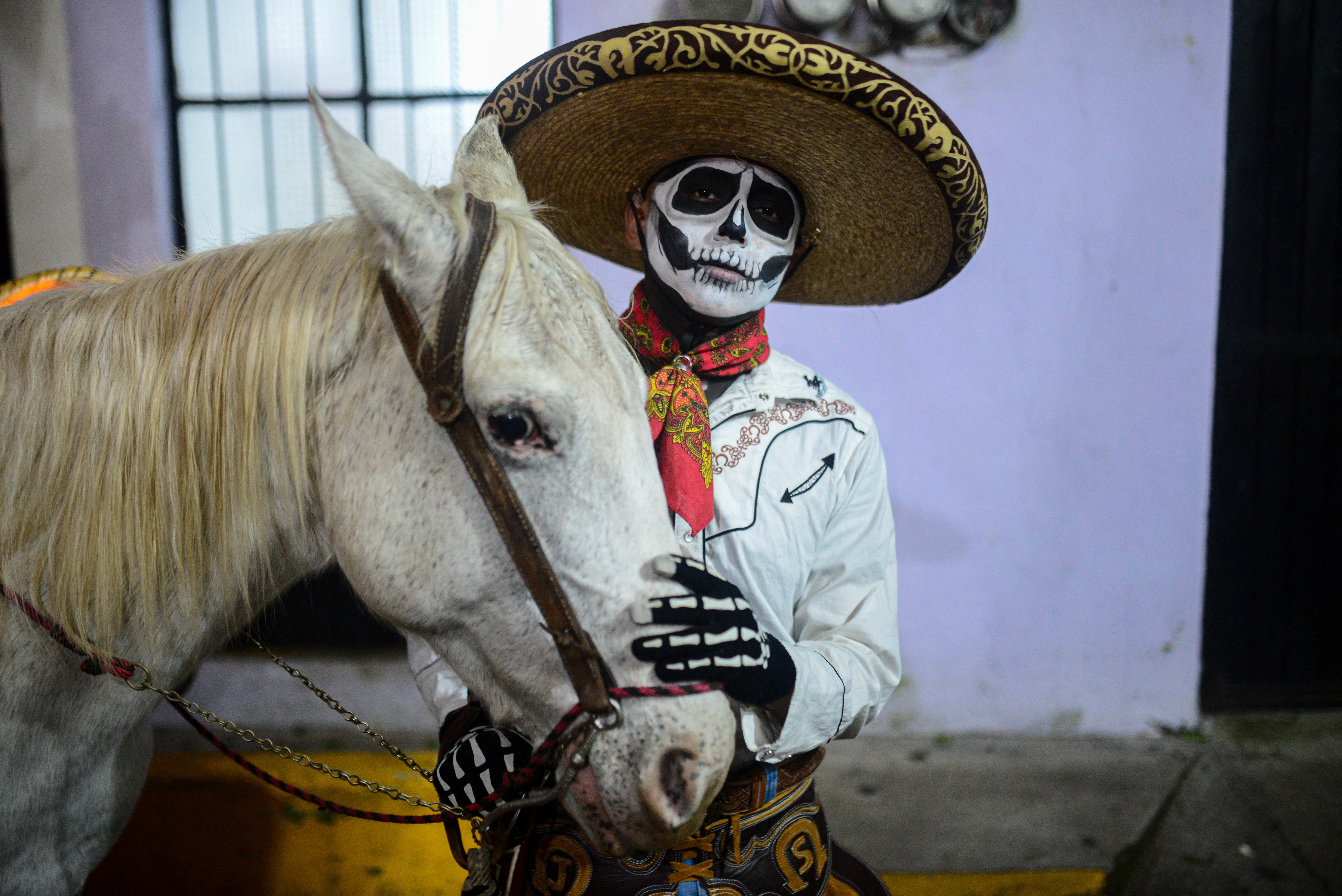 A man dressed and made up as a skeleton stands beside a horse.