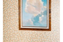 a cup in front of a painting of clouds against floral wallpaper