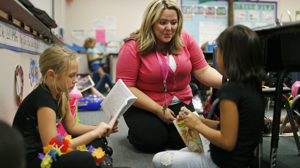 A substitute teacher sits on the floor with students as they read.