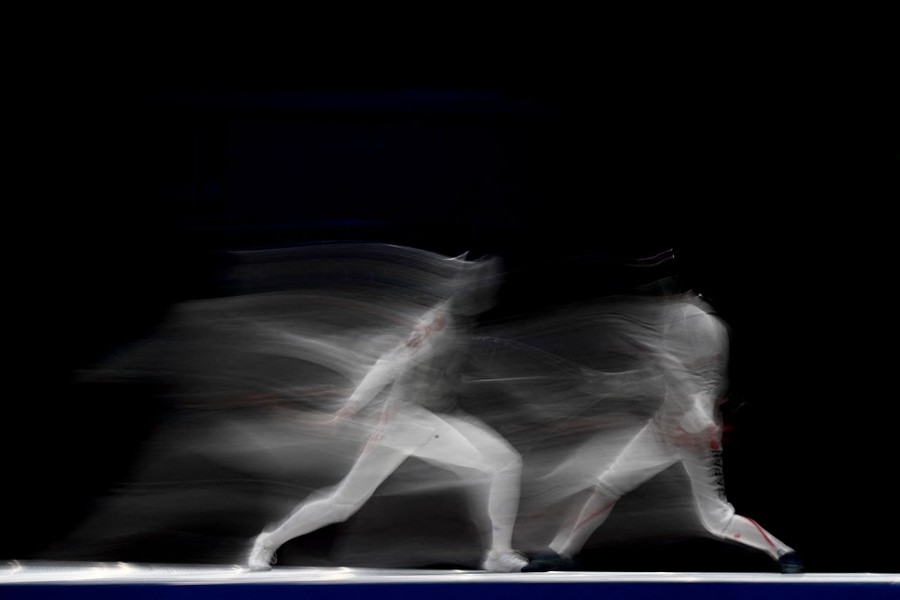 Two fencers compete, blurred in a long-exposure photo.