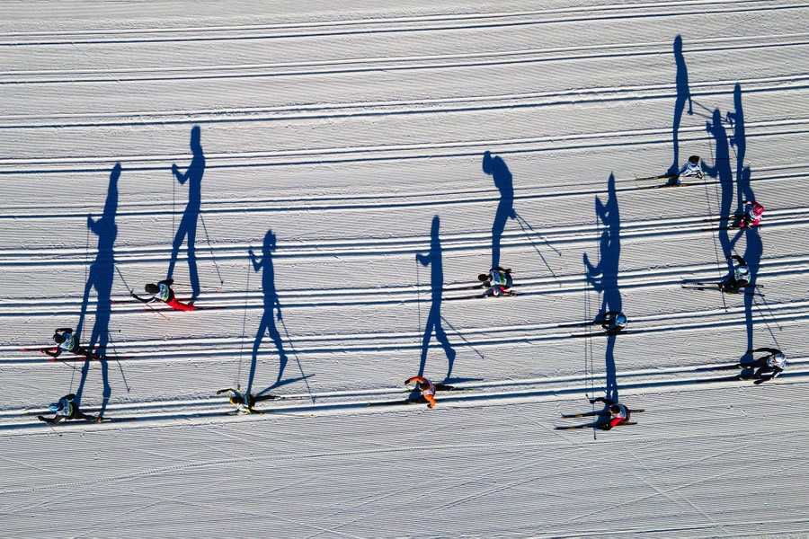 An aerial view, looking straight down, of cross-country skiers casting long shadows on the snow