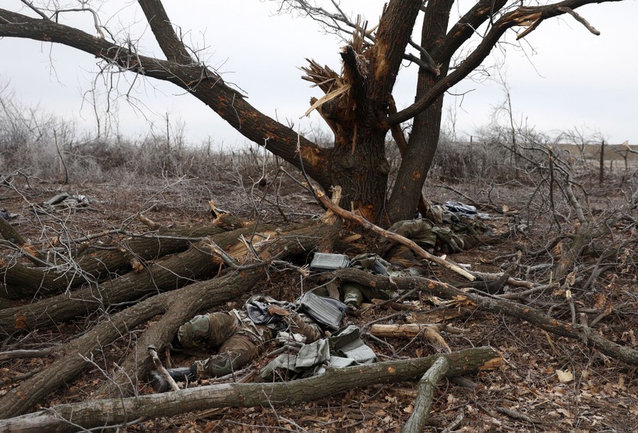 Large tree branches and the bodies of several soldiers lie beneath a damaged tree.