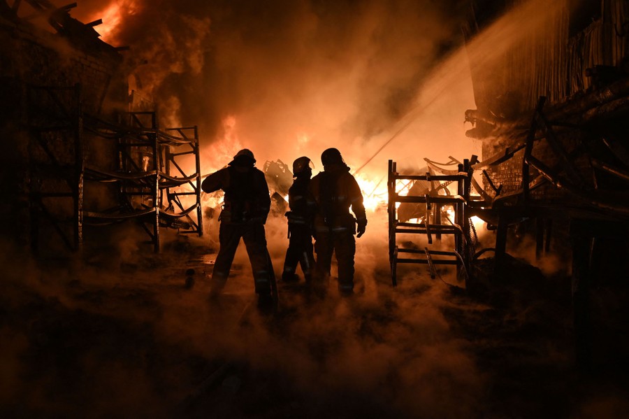 Several firefighters spray water on a fire inside an industrial building.