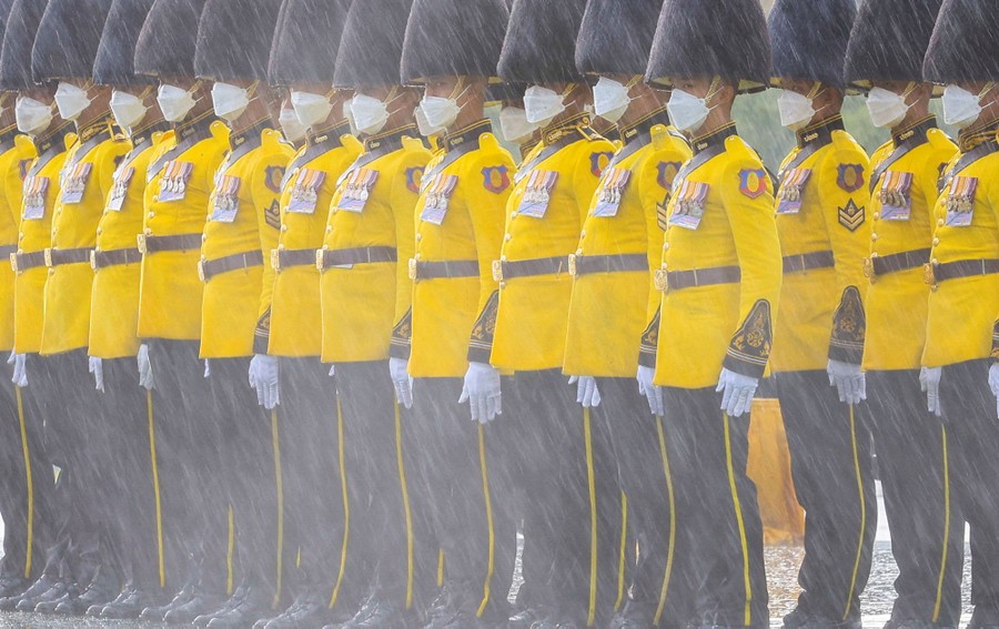 Soldiers in yellow dress uniforms and tall fuzzy hats stand at attention in a rainstorm.