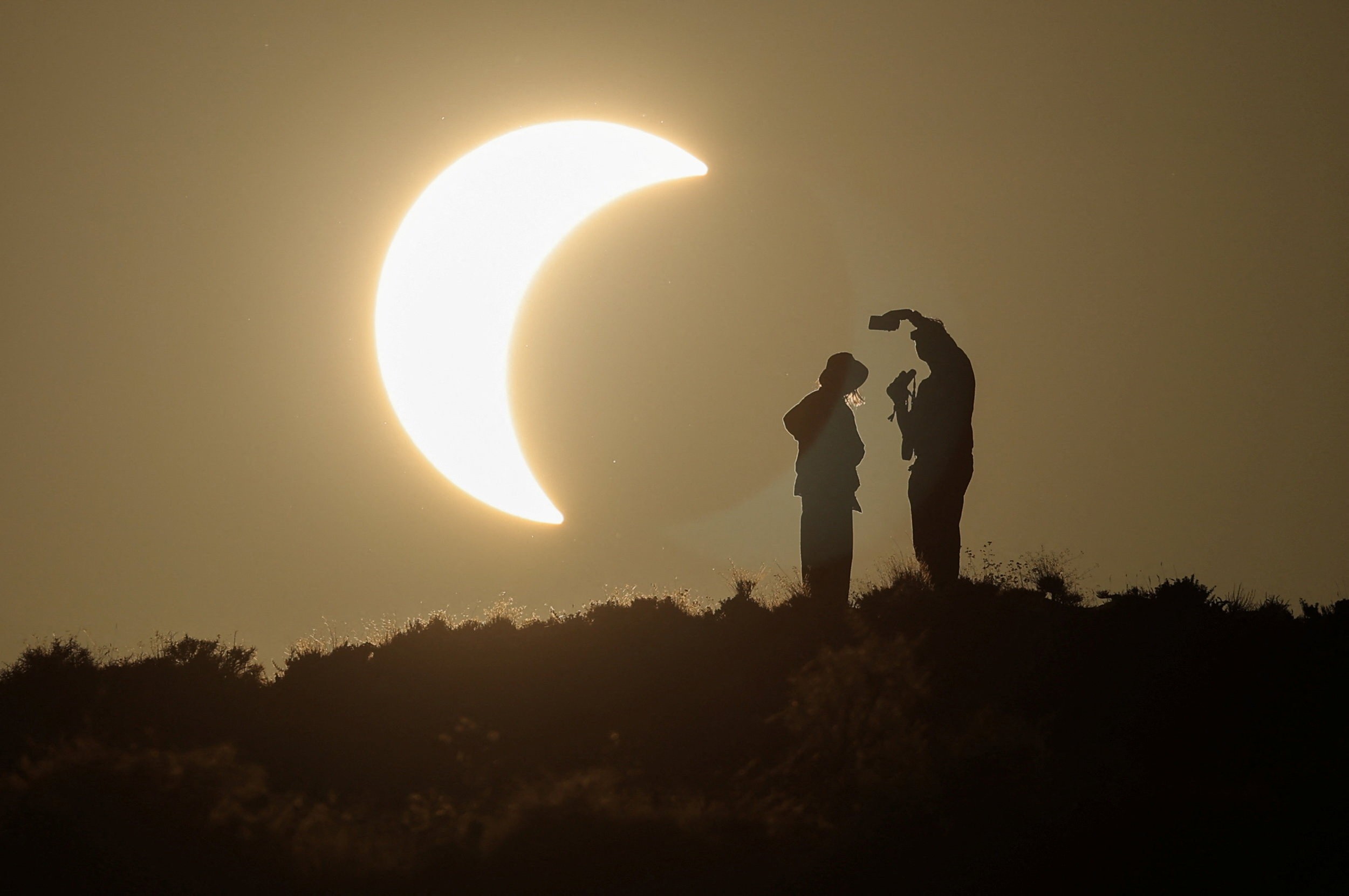 People stand on a hilltop, with a partial eclipse in the background.