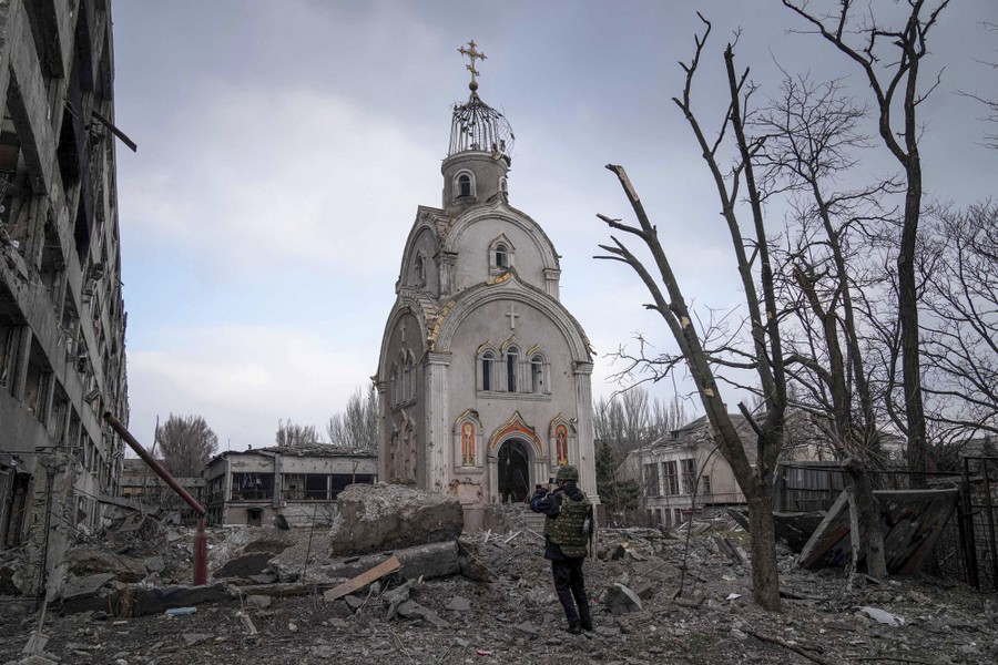 A soldier stands amid rubble in front of a damaged church building.
