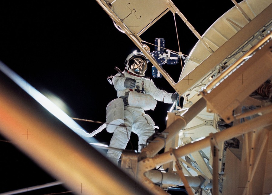 An astronaut wearing spacesuit works outside of a space station.