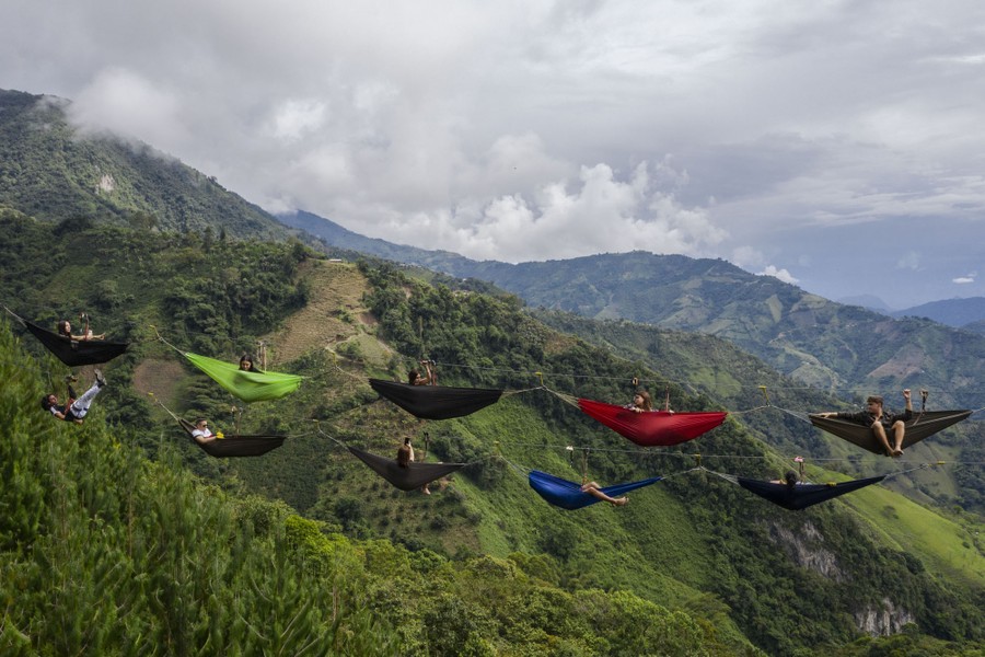 Ten people rest in hammocks hanging from two cables high above a steep valley.