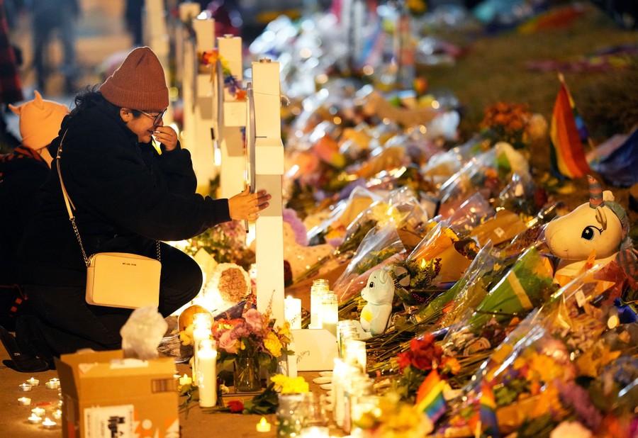 A woman kneels and cries at a cross at a makeshift memorial.