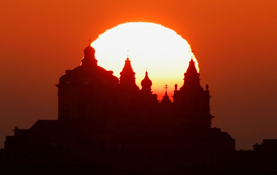 The sun rises behind a cathedral.