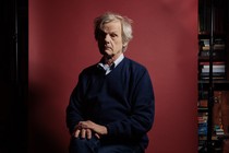 A man sits in a chair in front of a red backdrop