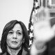 Black-and-white image of Kamala Harris looking at Joe Biden as he speaks in the foreground, his image blurred