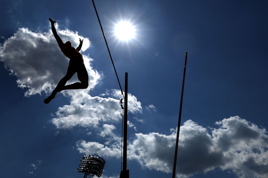 An athlete in silhouette as they fall toward a pad after completing a pole vault