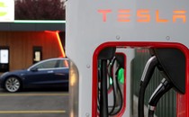A Tesla Supercharger in the foreground, with a car in the background