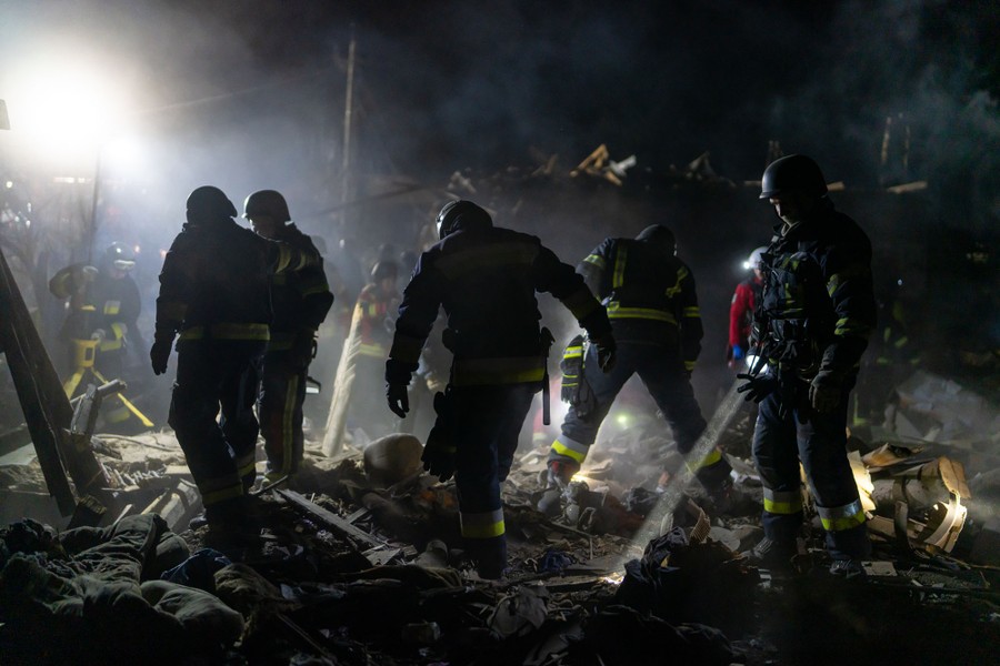 A group of firefighters work atop a pile of rubble at night.