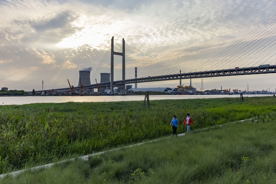 Two people walk on a path in a riverside park.