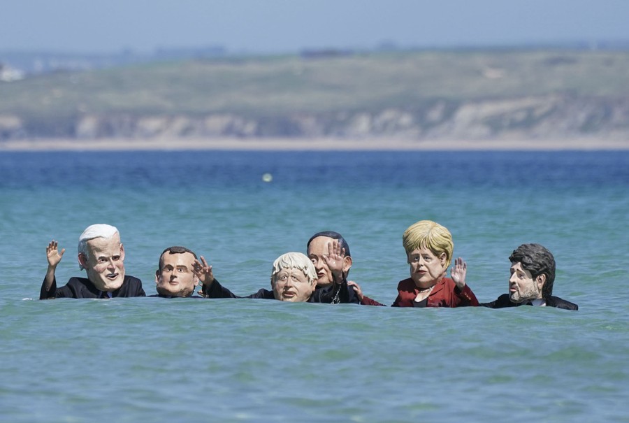 Six protesters stand in shoulder-deep water while wearing large full-head masks depicting world leaders.