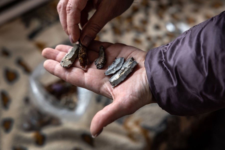 A person holds up five small pieces of shrapnel amid the ruins of a home.
