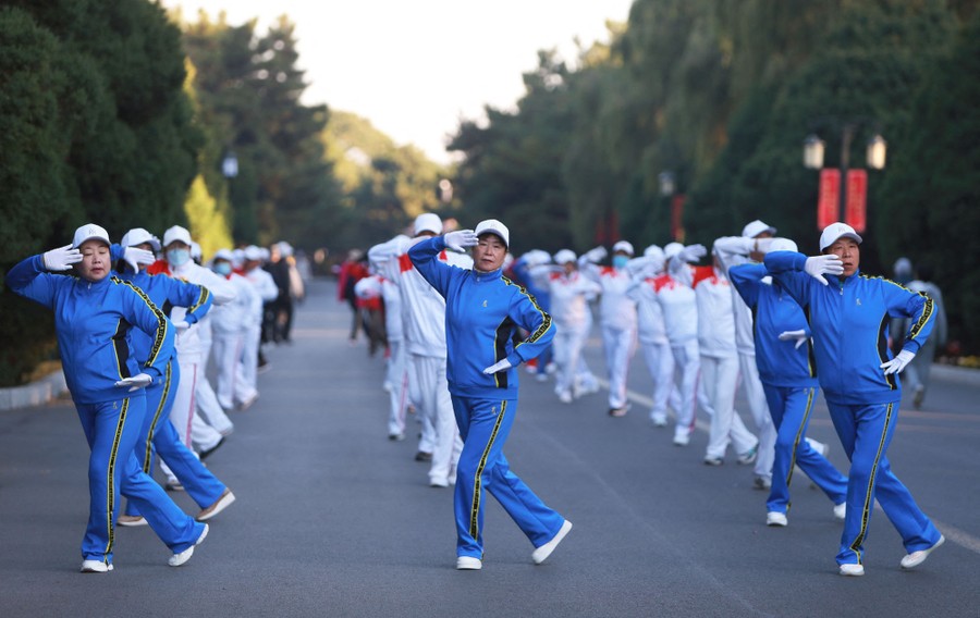 People in blue and white outfits dance together in three lines in a park.
