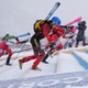 Three racers carrying skis on their backs run up a set of steps laid into a snow-covered mountain slope.