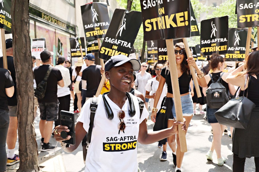 People march on a picket line, carrying signs that read "SAG-AFTRA on Strike!"