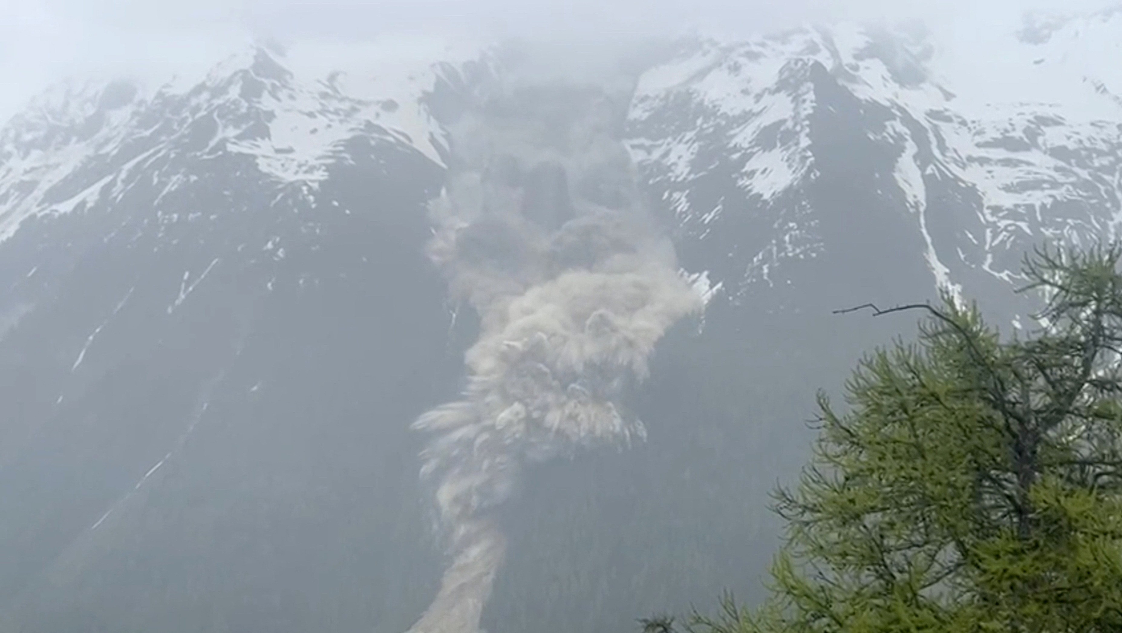 A screenshot from a video of a landslide explosively crashing down a mountainside.