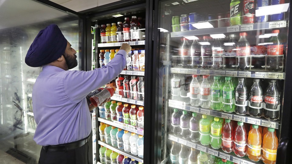A man selects a soft drink from a convenience-store refrigerator.