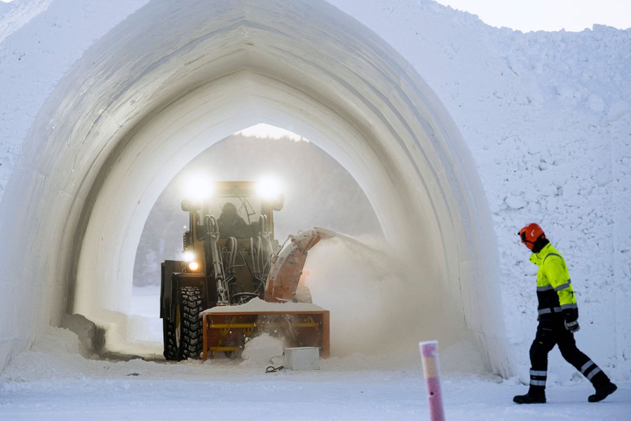 A tractor with a snowplow attachment works inside an arched hallway carved out of snow.