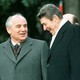 President Ronald Reagan stands with former Soviet leader Mikhail Gorbachev and laugh in front of an American flag.