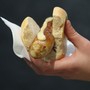 A hand holding a rostbratwurst pork sausage with mustard on top of it 