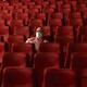 A man wearing a mask sits alone in a theater.