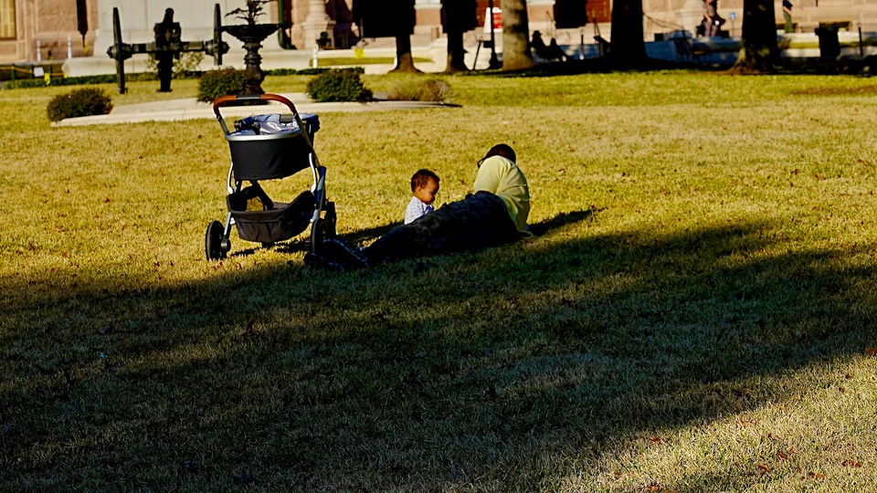 A father and small child relax on the grass.