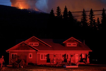 A house in Lytton glows red as a wildfire burns in the background.