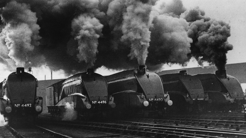 Five black steam engines blow smoke into the air.