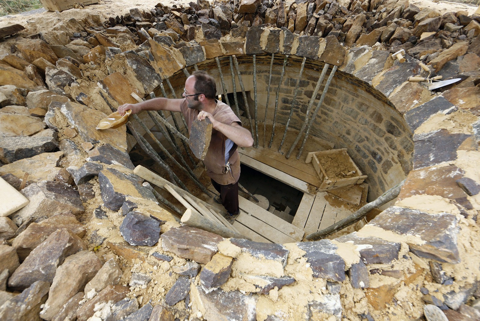 A stoneworker pours water onto stones and mortar being placed in a circle atop a round chamber.