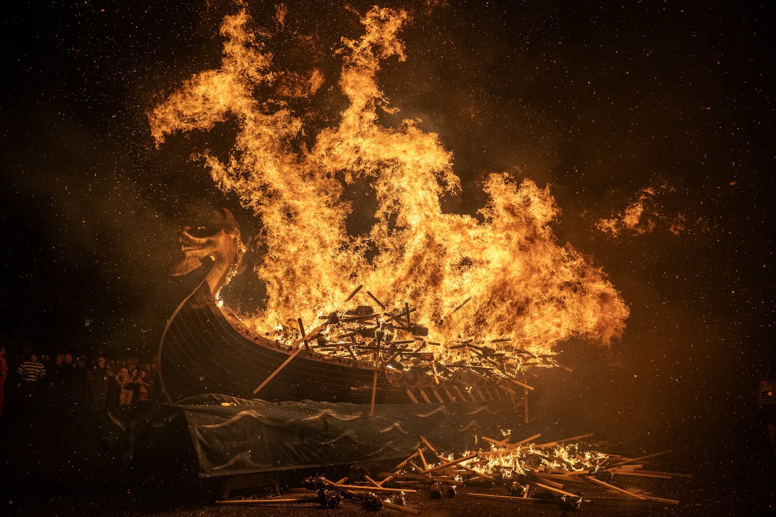 A replica of a Viking ship goes up in flames, surrounded by piles of burning torches.