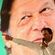 Imran Khan holds a microphone while standing in front of a backdrop with a photograph of his face at a campaign rally