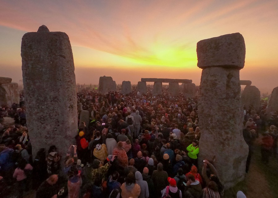 Hundreds of people stand together inside Stonehenge at sunrise.