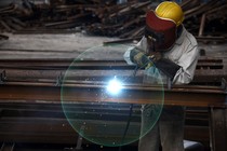 Someone works in a factory. The worker's face is covered with a protective helmet. A flash of light flickers.