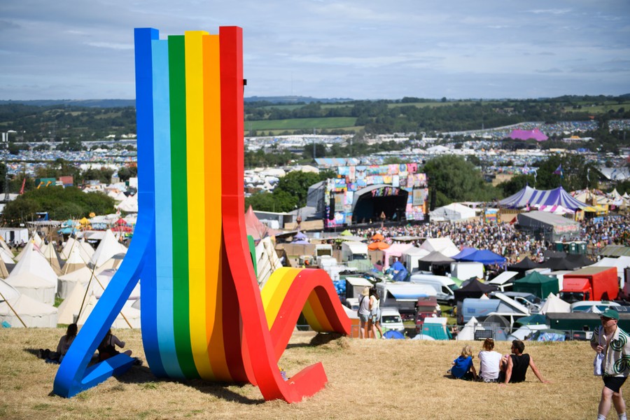 A rainbow-colored, chair-shaped sculpture looks over festival grounds in a rural area.