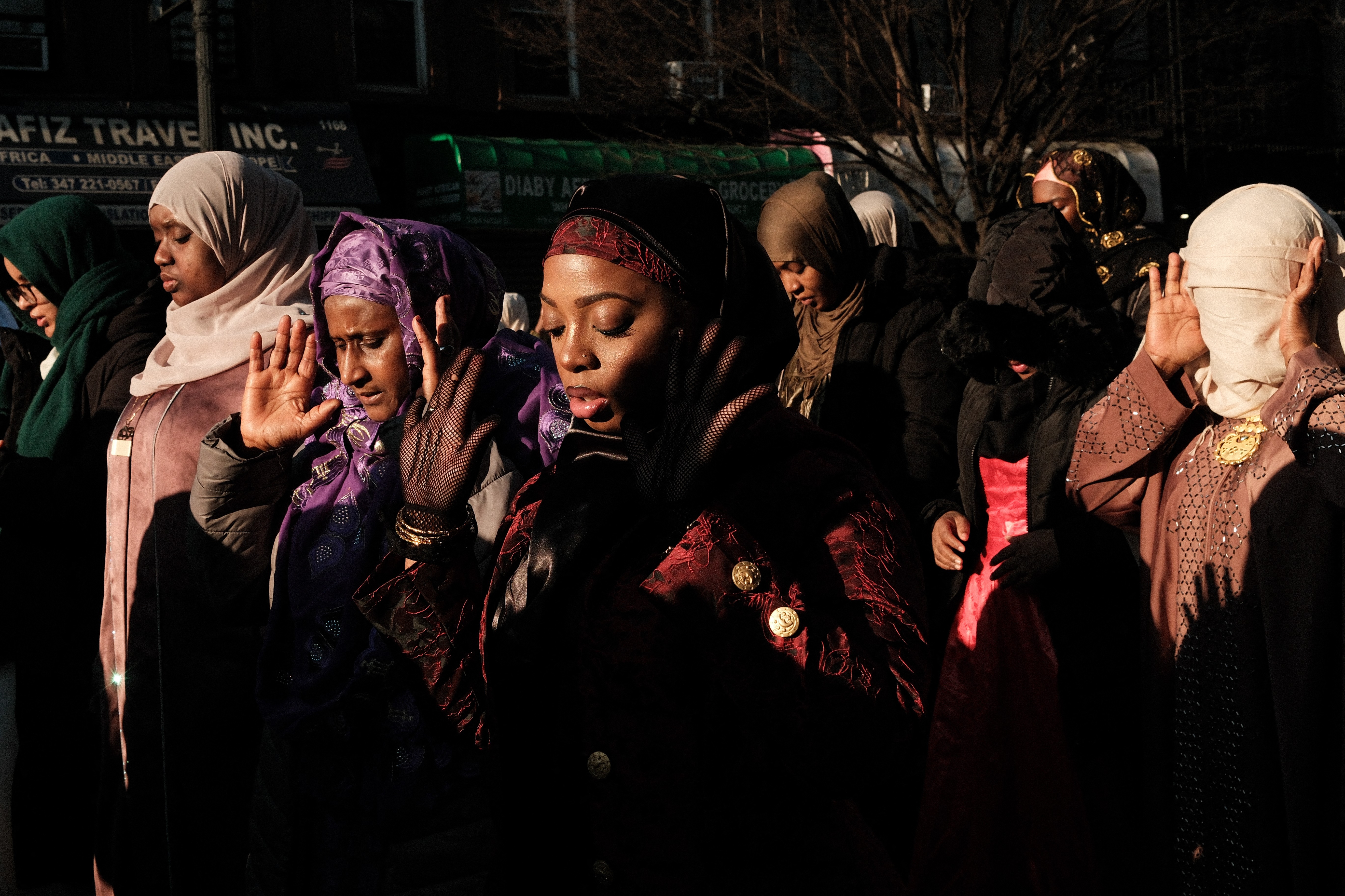 A group of people stand side-by-side outside a mosque, praying together.