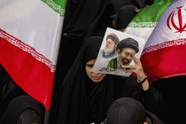 A photo of an Iranian holding a flyer picturing two supreme leaders