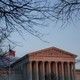 The Supreme Court (and American flag next to it) are slightly pink in a sunset, and framed by leaf-less trees.