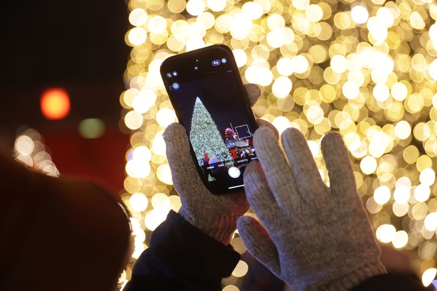 A visitor with a smartphone photographs an illuminated Christmas tree.