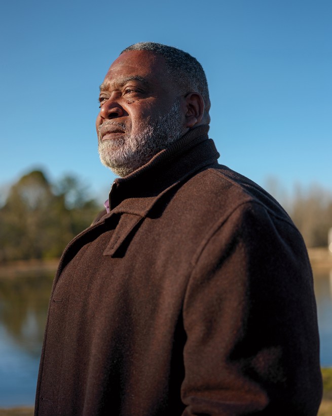 photo of bearded man wearing brown jacket with blue sky and trees in background