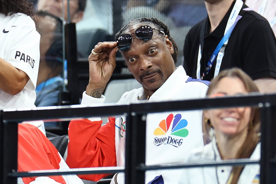 Snoop Dogg raises his dark glasses for a better look, while sitting in the stands of an arena.
