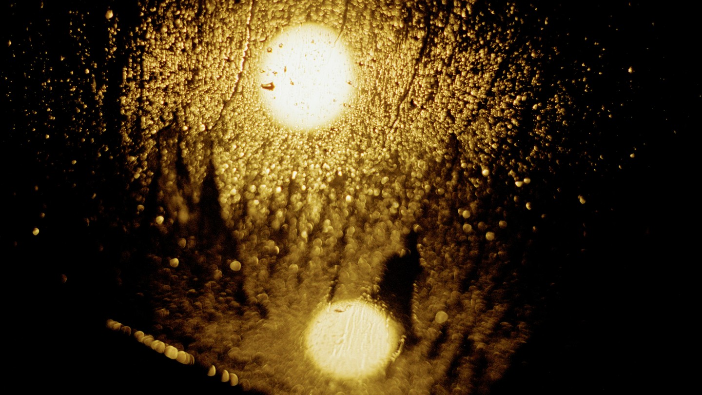 A yellow light shines through a glass with raindrops on it.