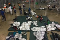 Children lie on green mattresses on the floor and use silver space blankets.