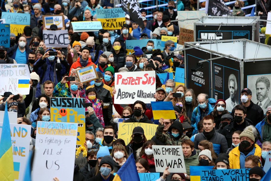 A large crowd of people can be seen marching, carrying handwritten signs protesting Russia's invasion of Ukraine.