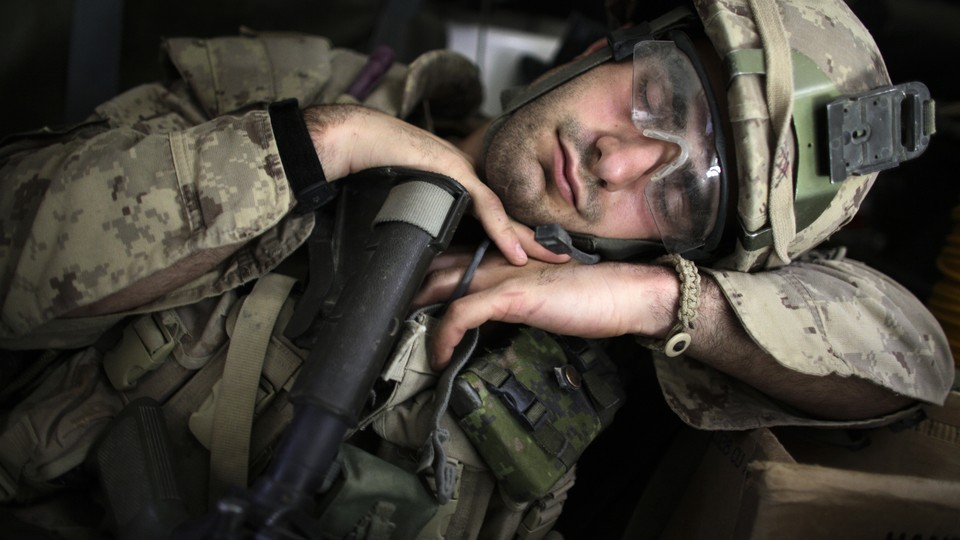 A soldier sleeping in uniform while leaning on his weapon